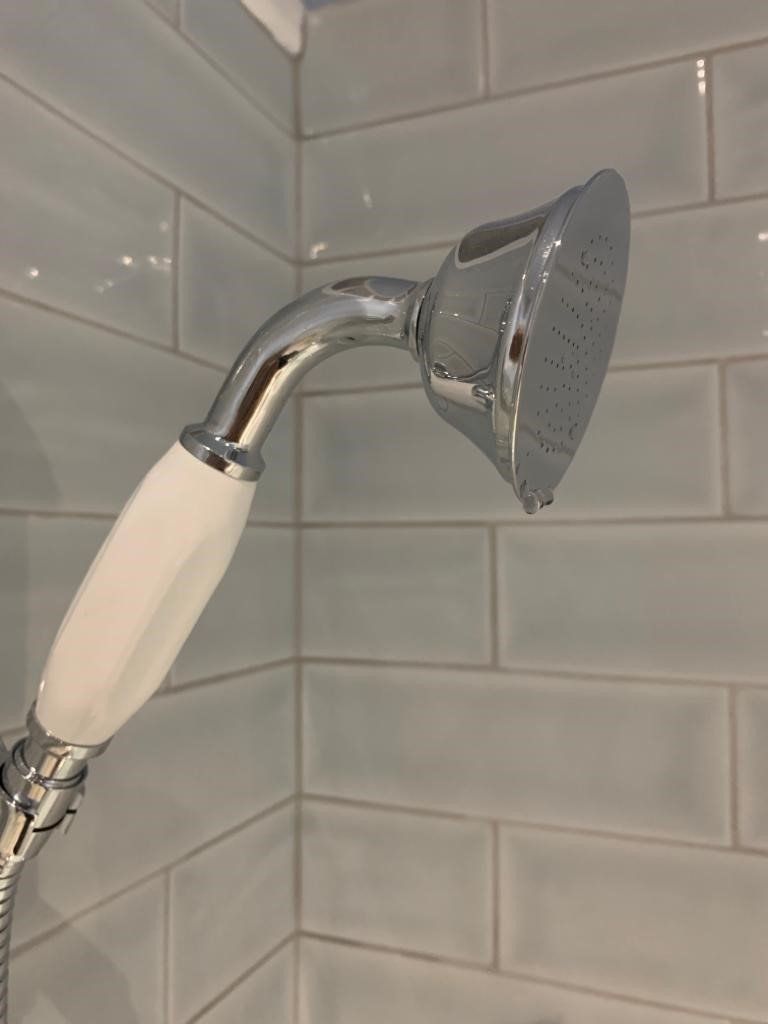 Chrome handheld shower head with white handle against light blue bathroom tiles
