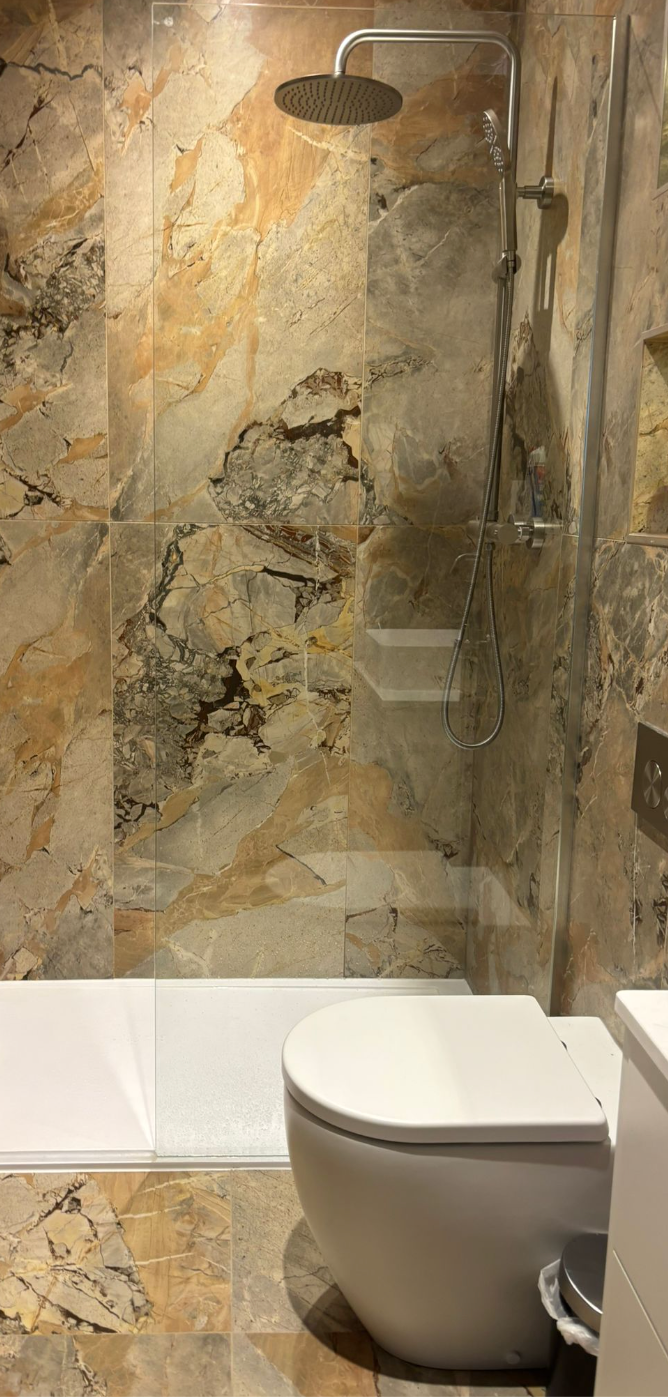 Modern bathroom with a stone-tiled shower, rainfall showerhead, and toilet in the foreground