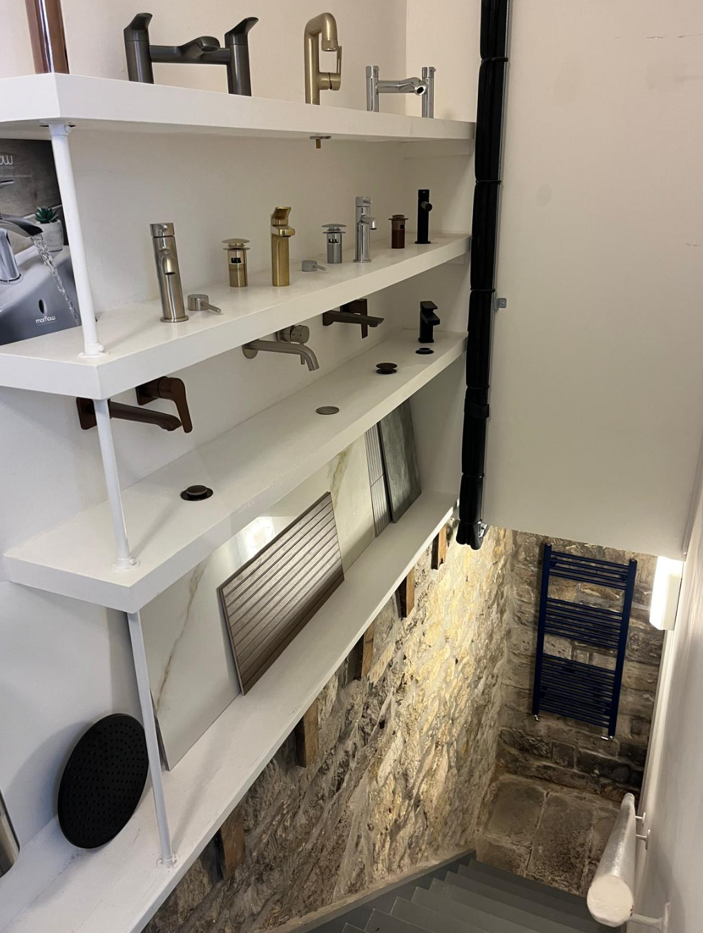 White shelves with small metal fixtures overlook a narrow staircase and stone wall in a stairwell.