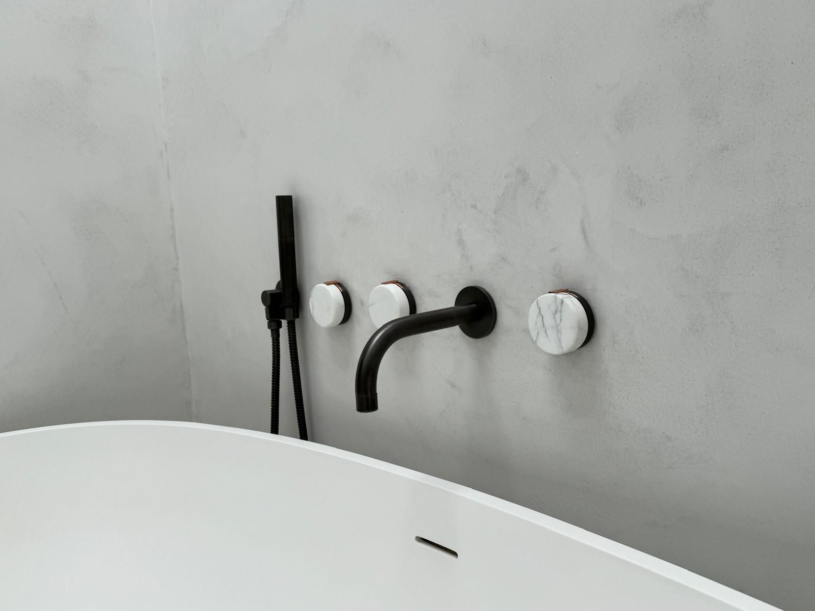 Minimal bathroom wall with black shower fixtures and three white wall caps above a white tub edge