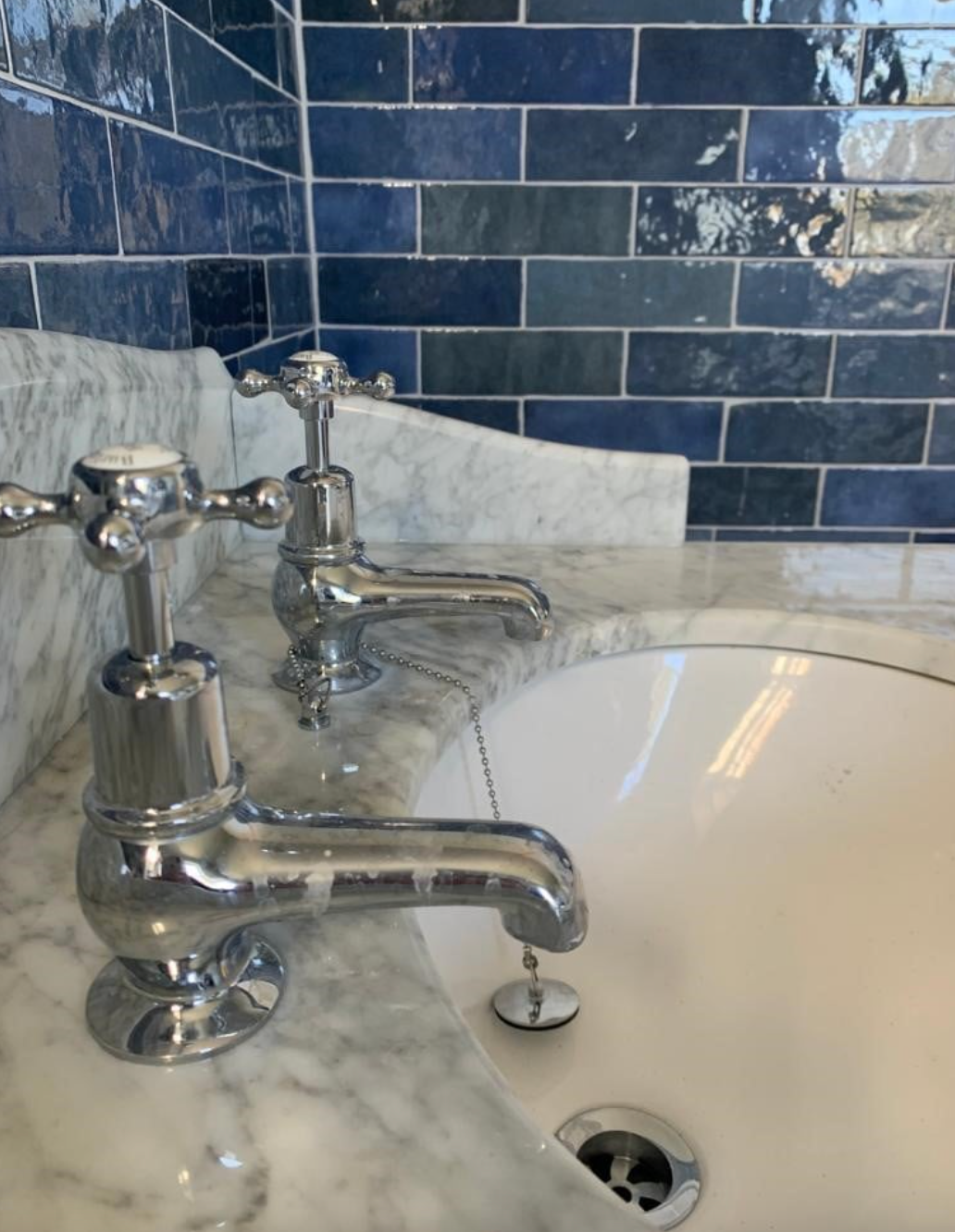 Chrome faucet and white marble sink with blue tile backsplash in a bathroom