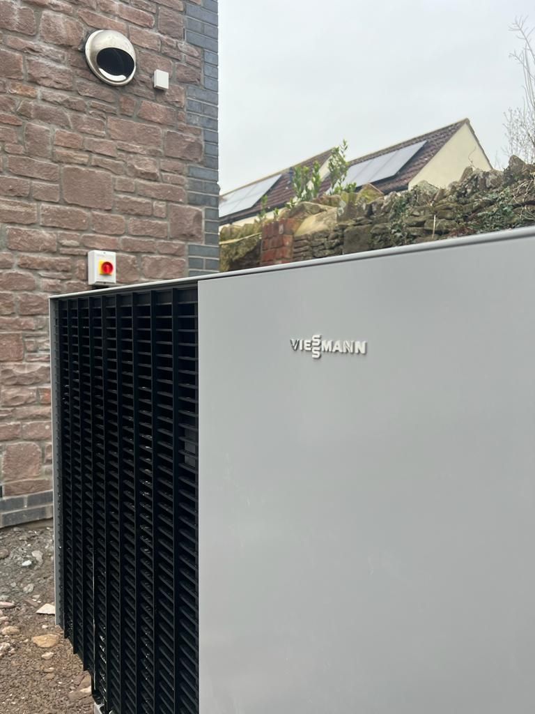 Outdoor Viessmann heat pump beside a brick wall with a round vent and nearby house roofline