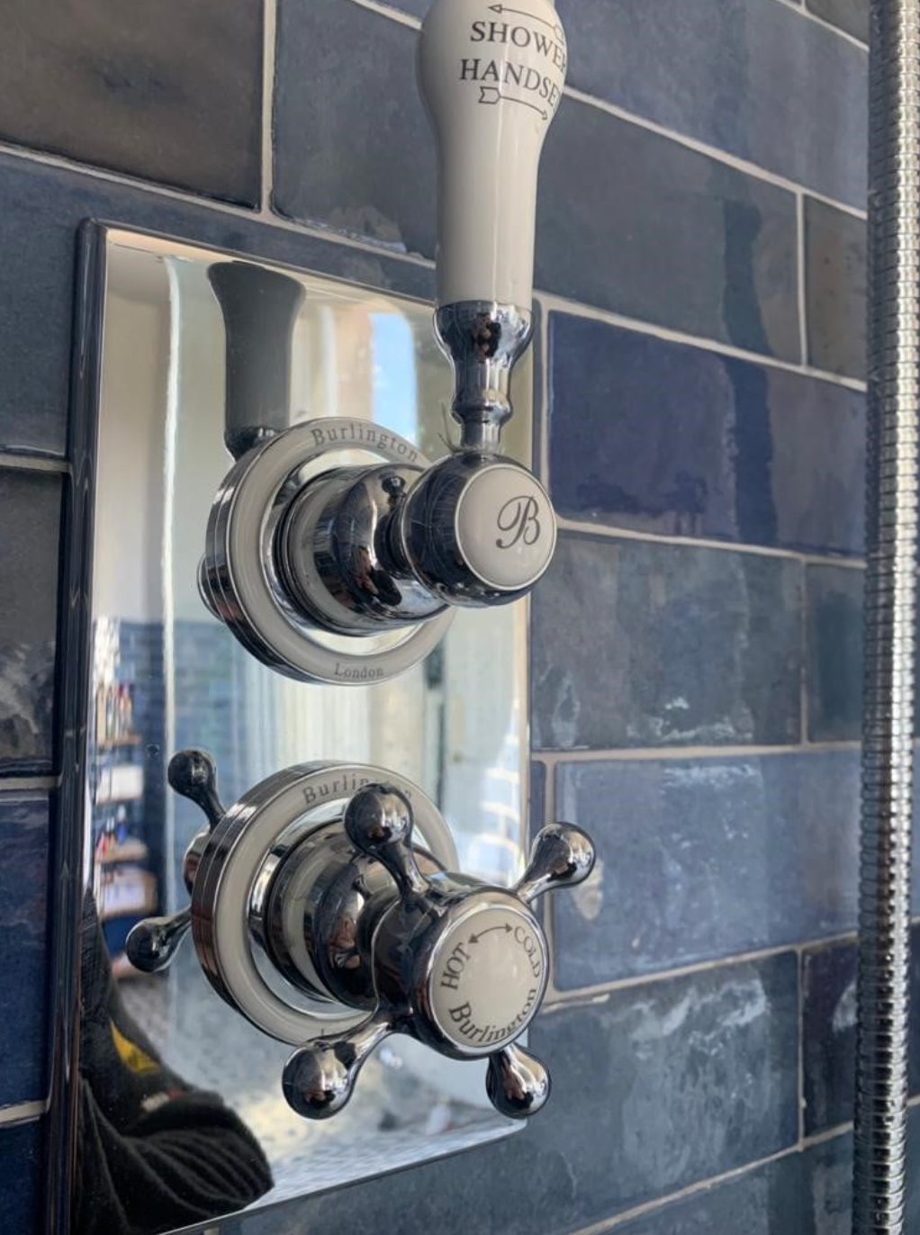 Chrome shower control panel with two vintage-style knobs on blue tiled wall