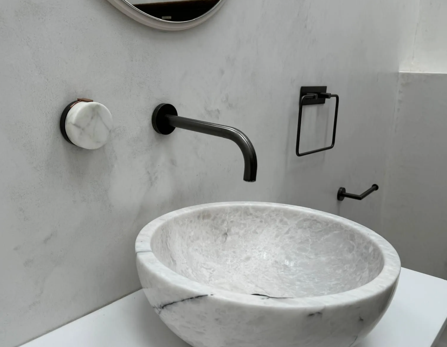Modern bathroom with a white stone sink, black faucet, towel ring, and toilet paper holder