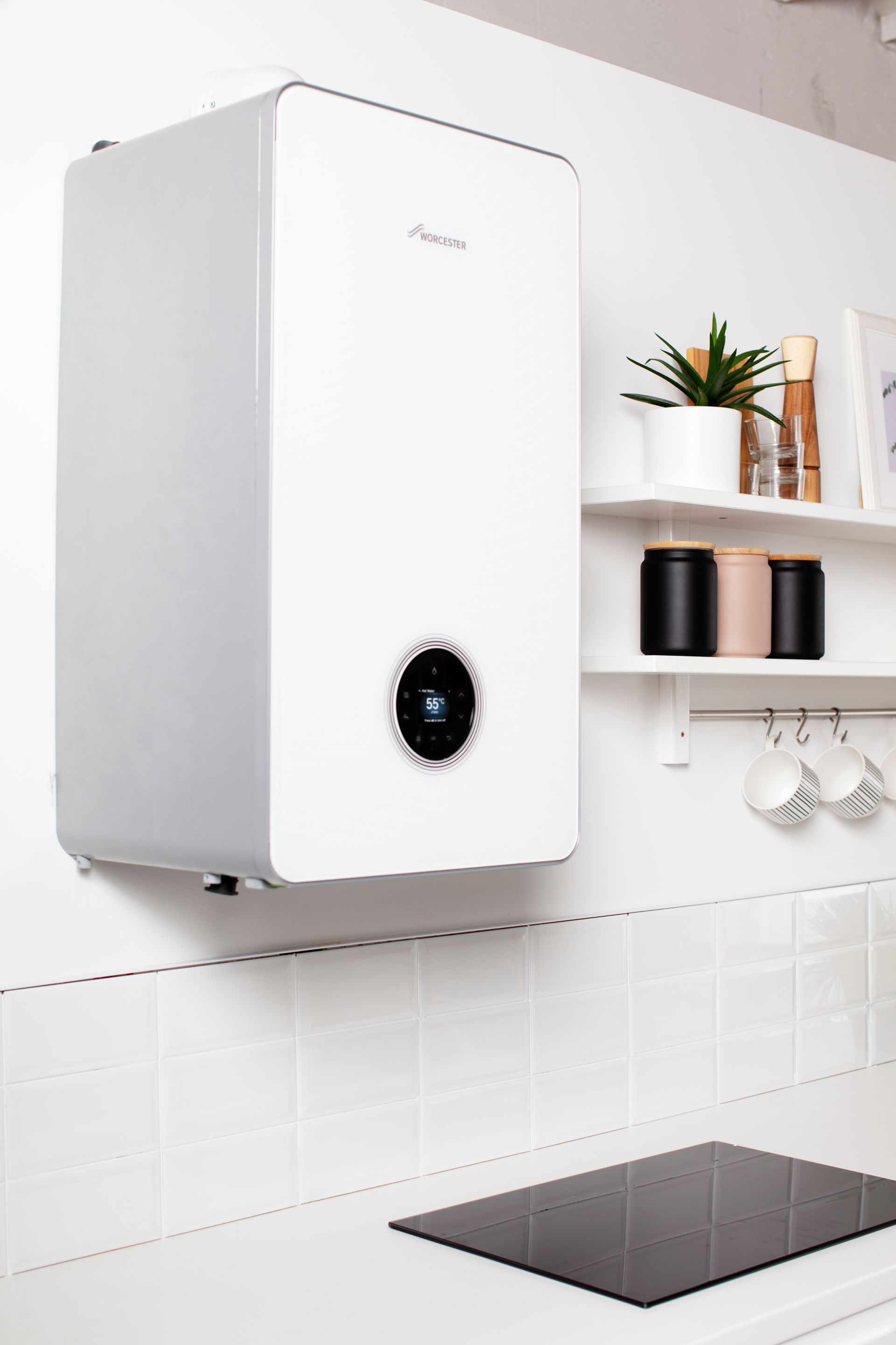 White wall-mounted boiler above a kitchen stovetop in a modern kitchen with shelves and plants