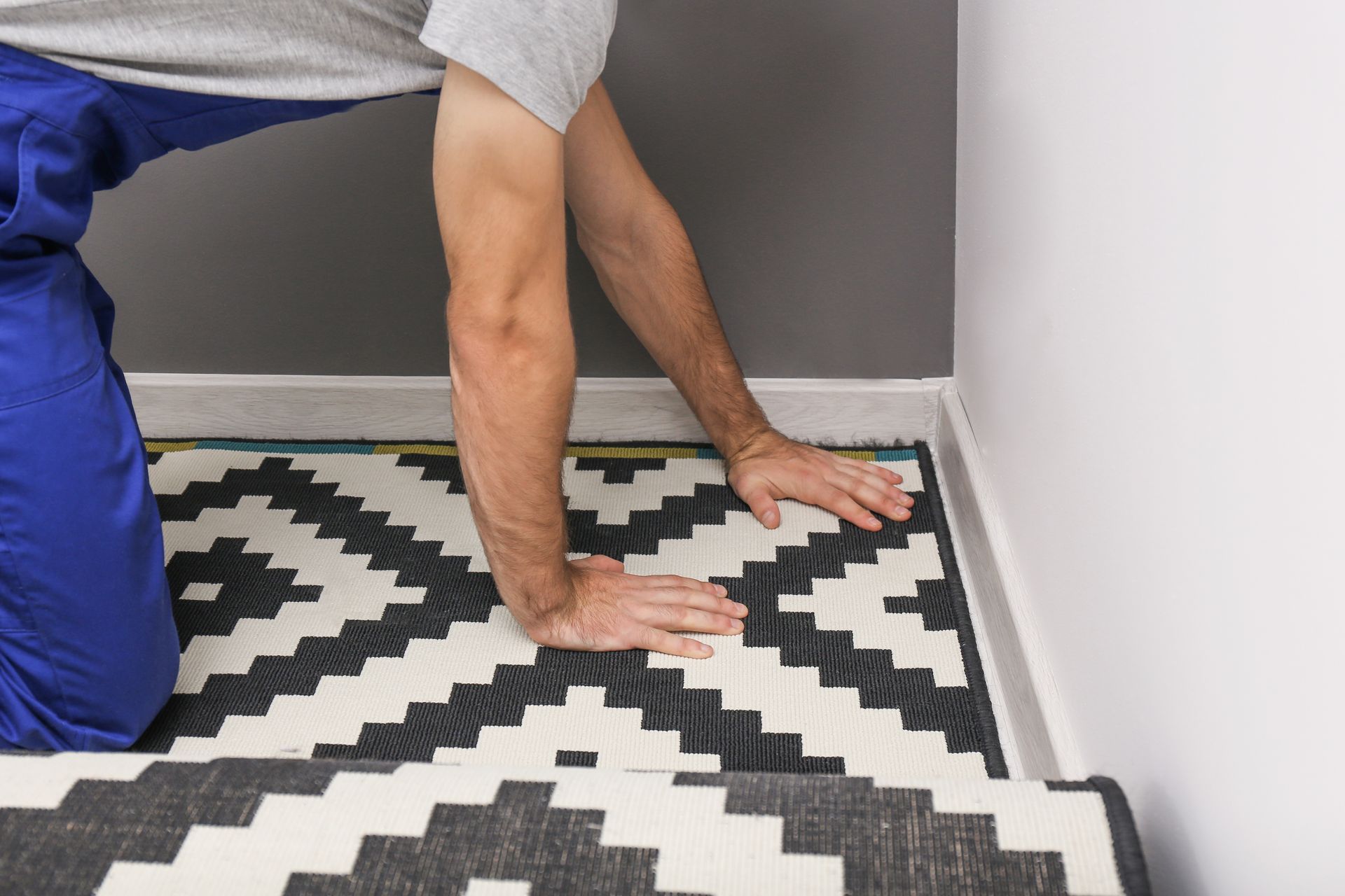 Person kneeling and installing a patterned rug, pressing it firmly into place