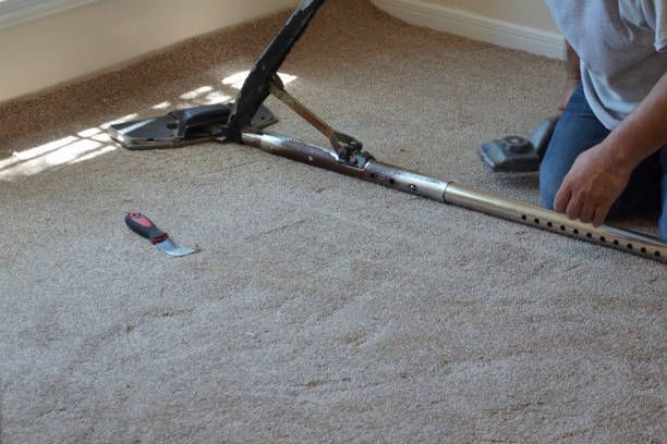 Construction worker installing new carpet with tools.
