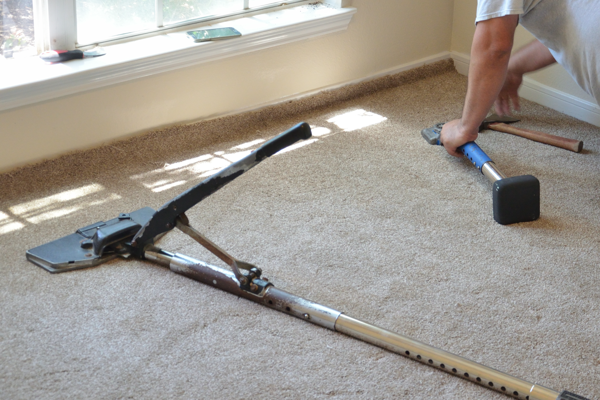 A person installing carpet using a knee kicker and a carpet stretcher.