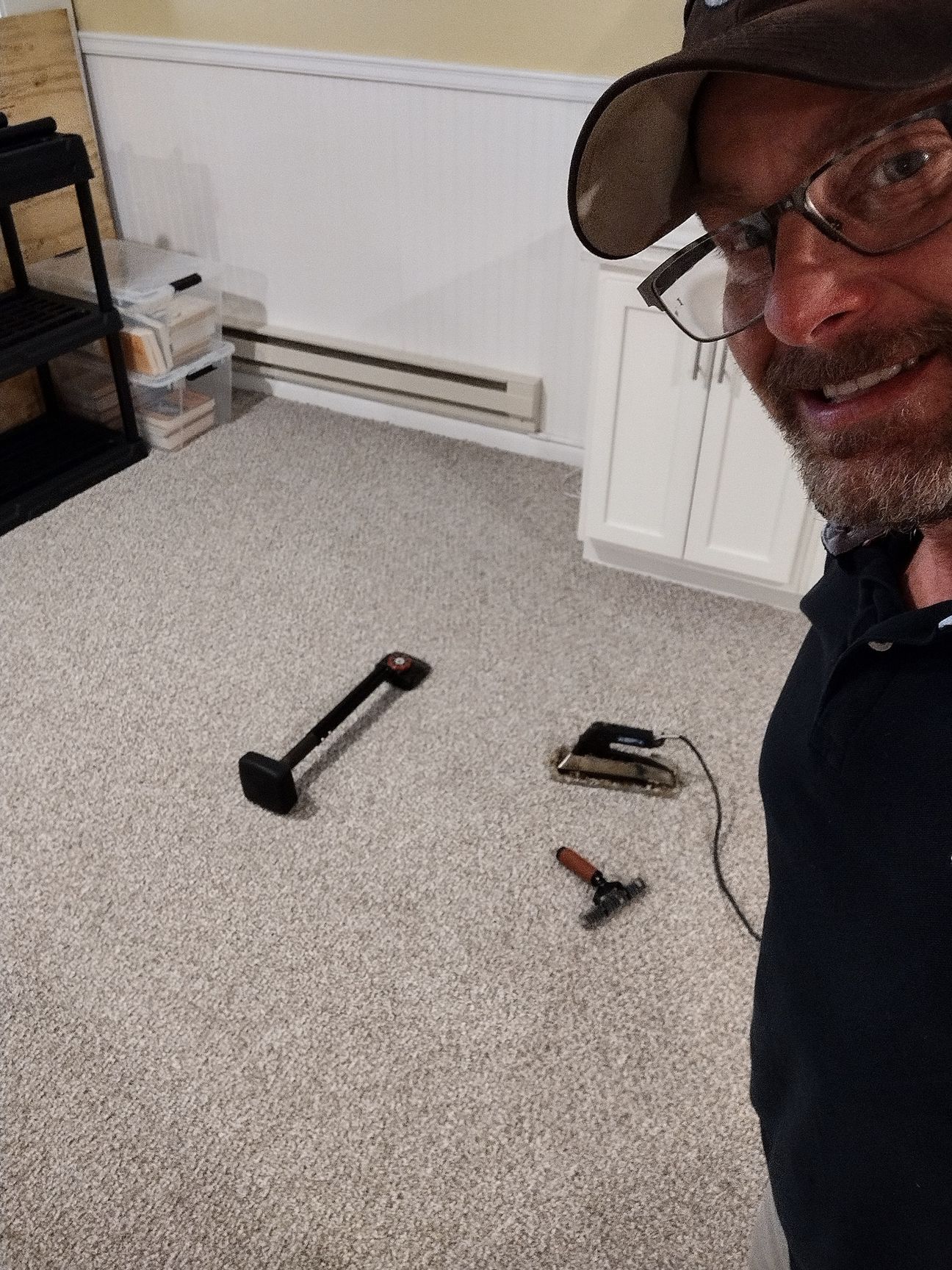 Man smiles for a selfie in a room with new carpet and tools on the floor.