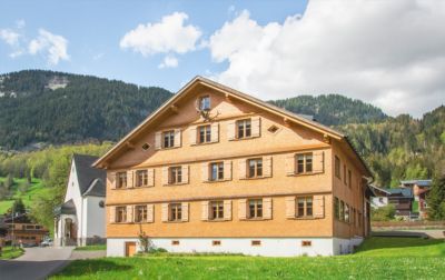 Ein großes Holzhaus mit einer Kirche im Hintergrund und Bergen im Hintergrund.