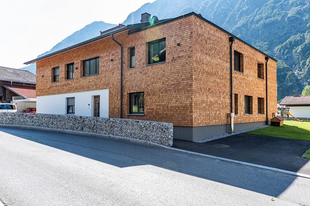 Ein großes Backsteingebäude mit einem Steinzaun davor und Bergen im Hintergrund.