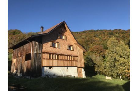 Auf der Spitze eines Hügels steht ein großes Holzhaus, umgeben von Bäumen.