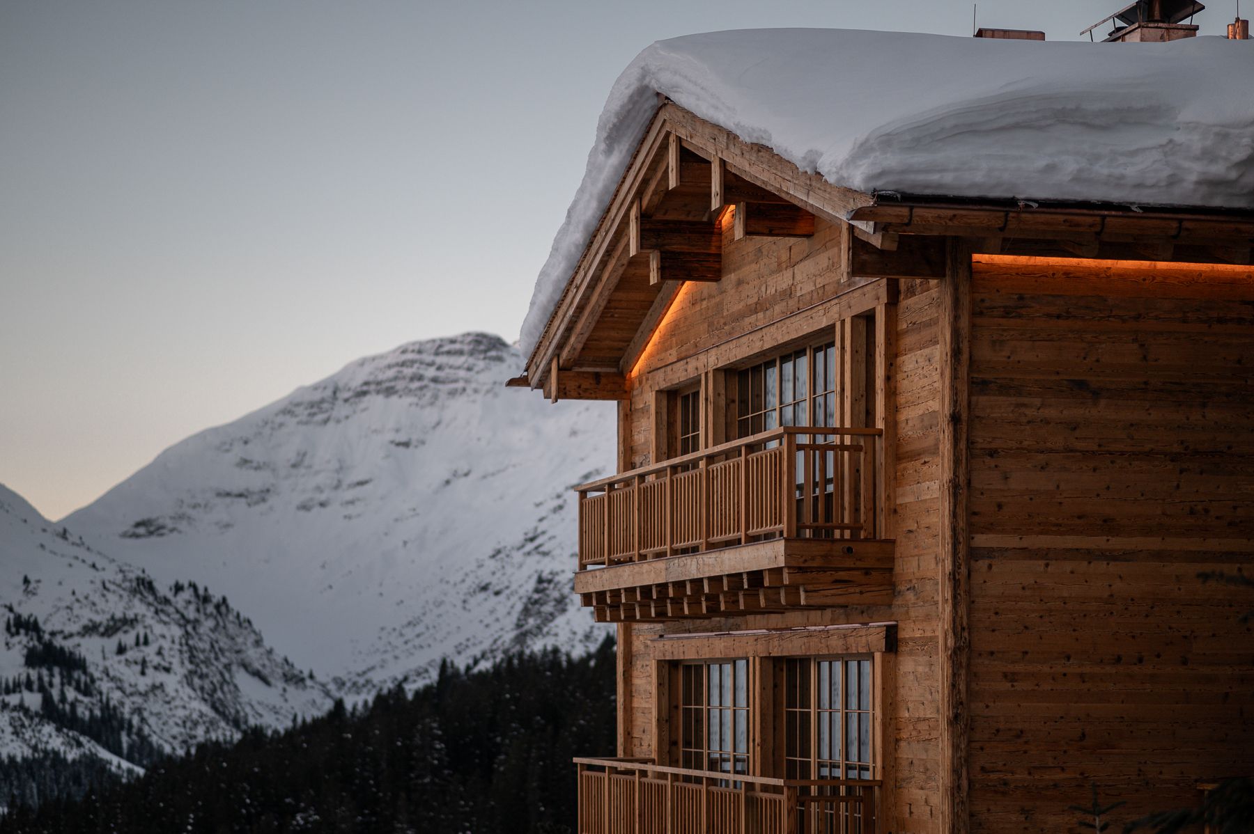 Ein Holzhaus mit Schnee auf dem Dach ist von schneebedeckten Bergen umgeben.