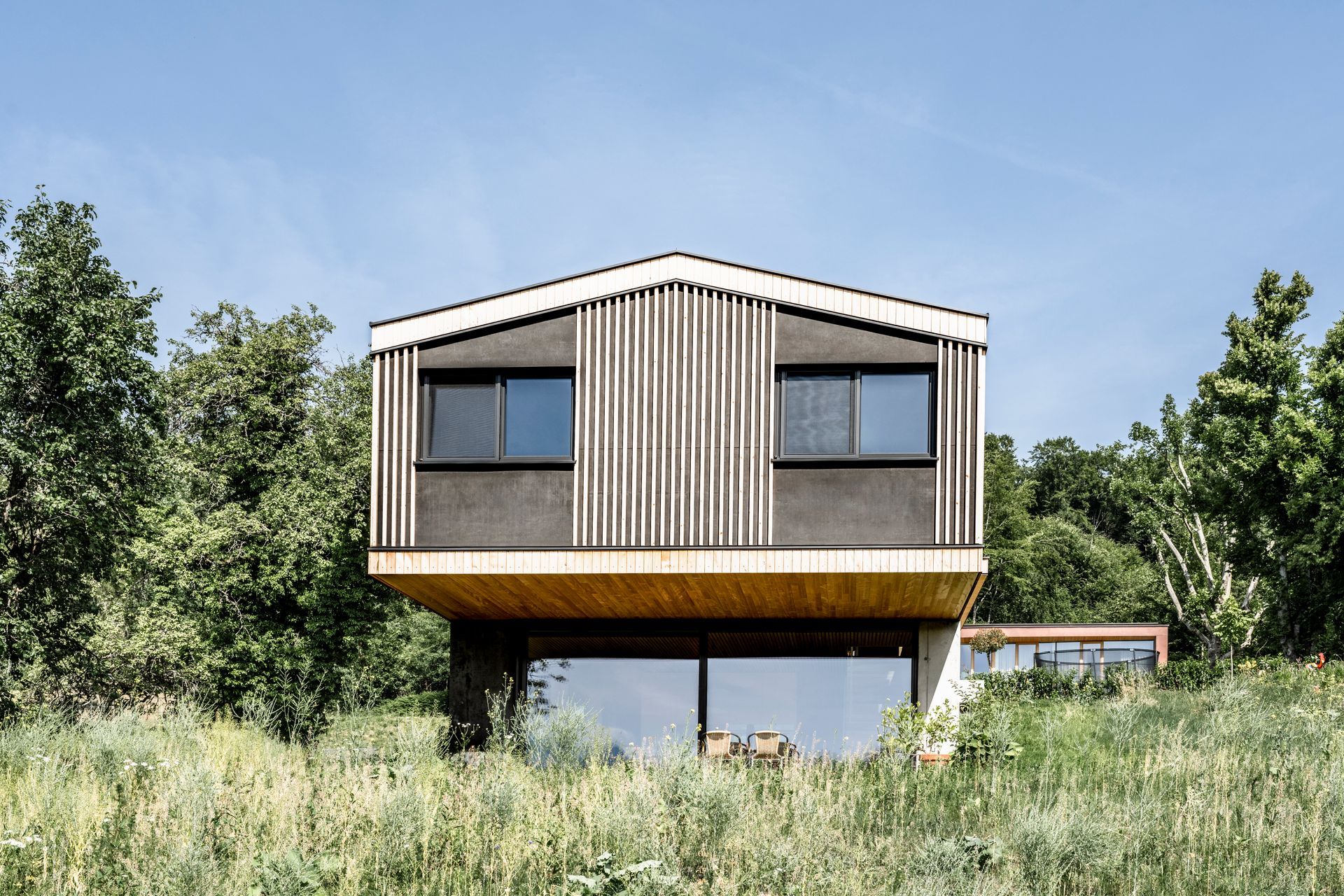 Auf einem grasbewachsenen Hügel steht ein Haus, umgeben von Bäumen.