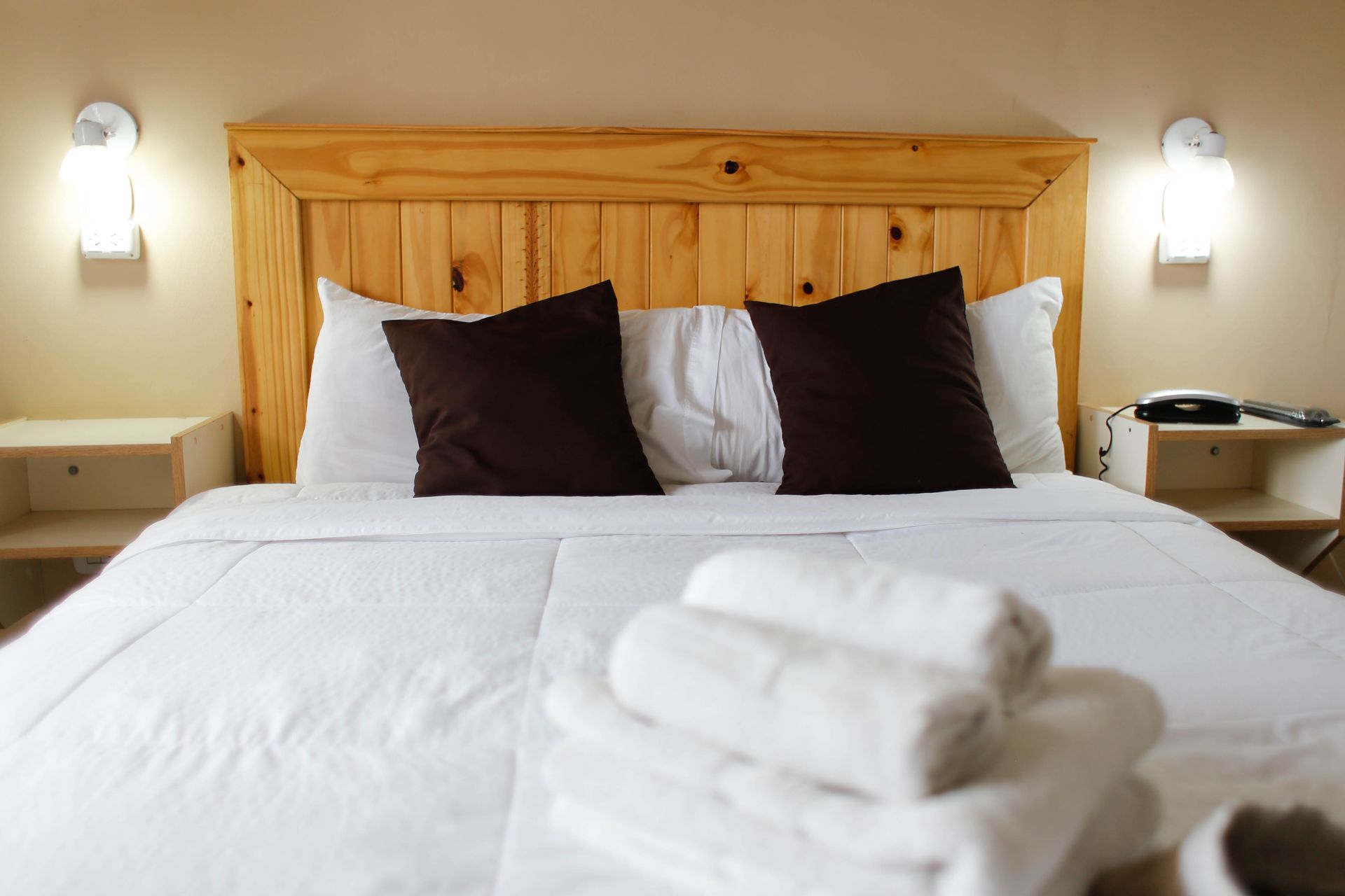 Una cama con sábanas blancas y almohadas marrones en una habitación de hotel.