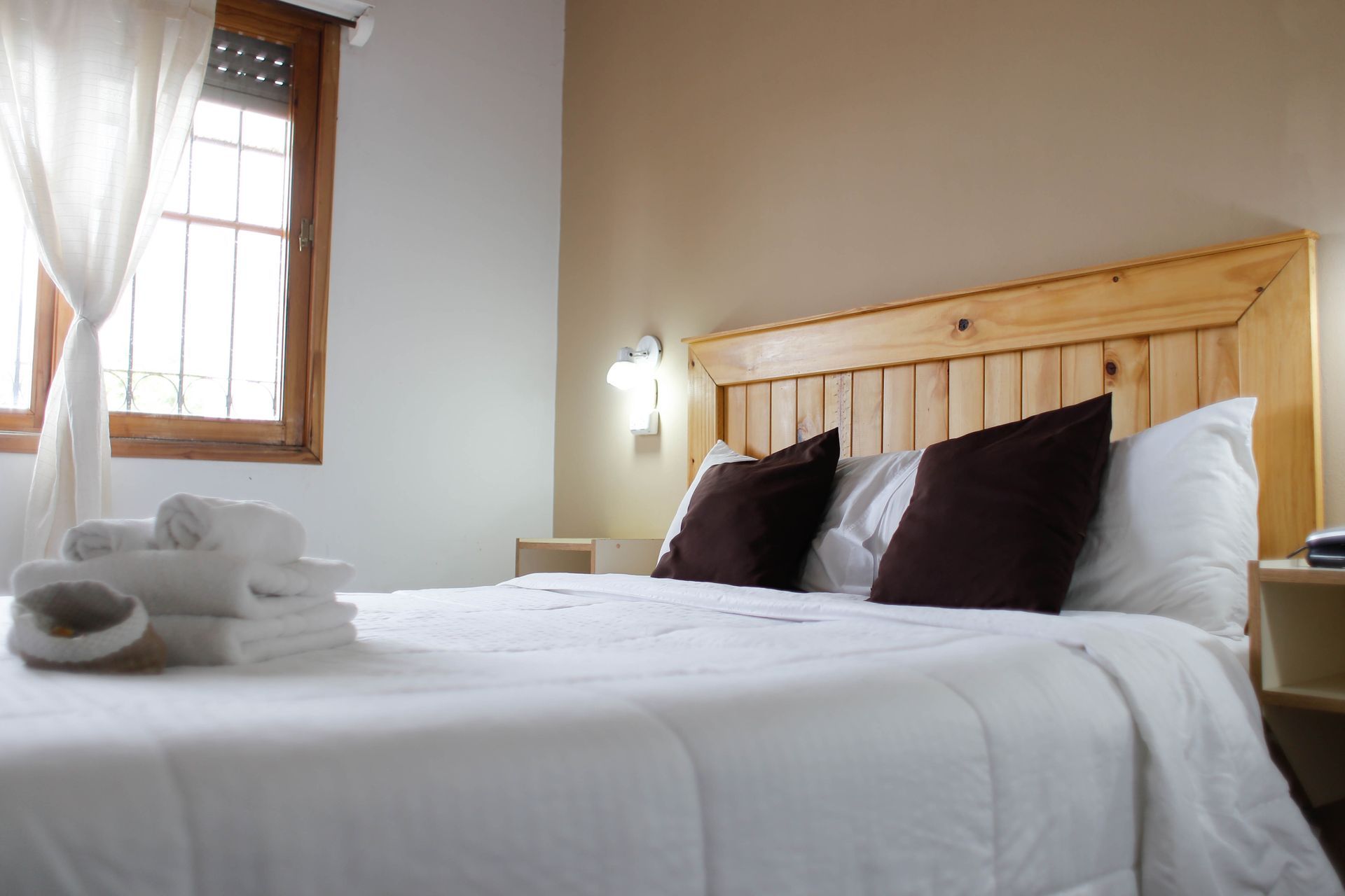 Una cama con sábanas blancas y almohadas marrones en una habitación de hotel