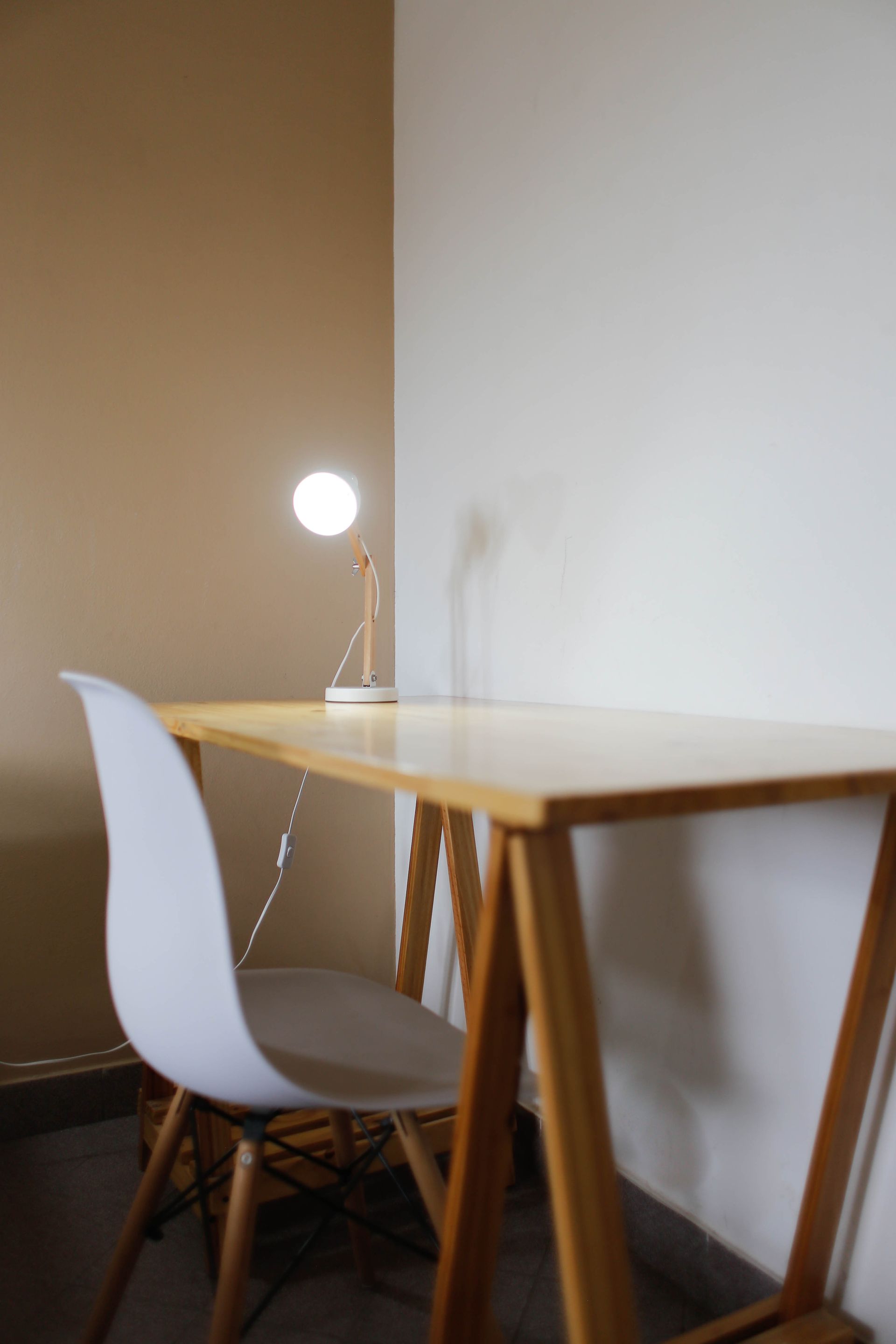 Un escritorio de madera con una silla blanca y una lámpara encima.