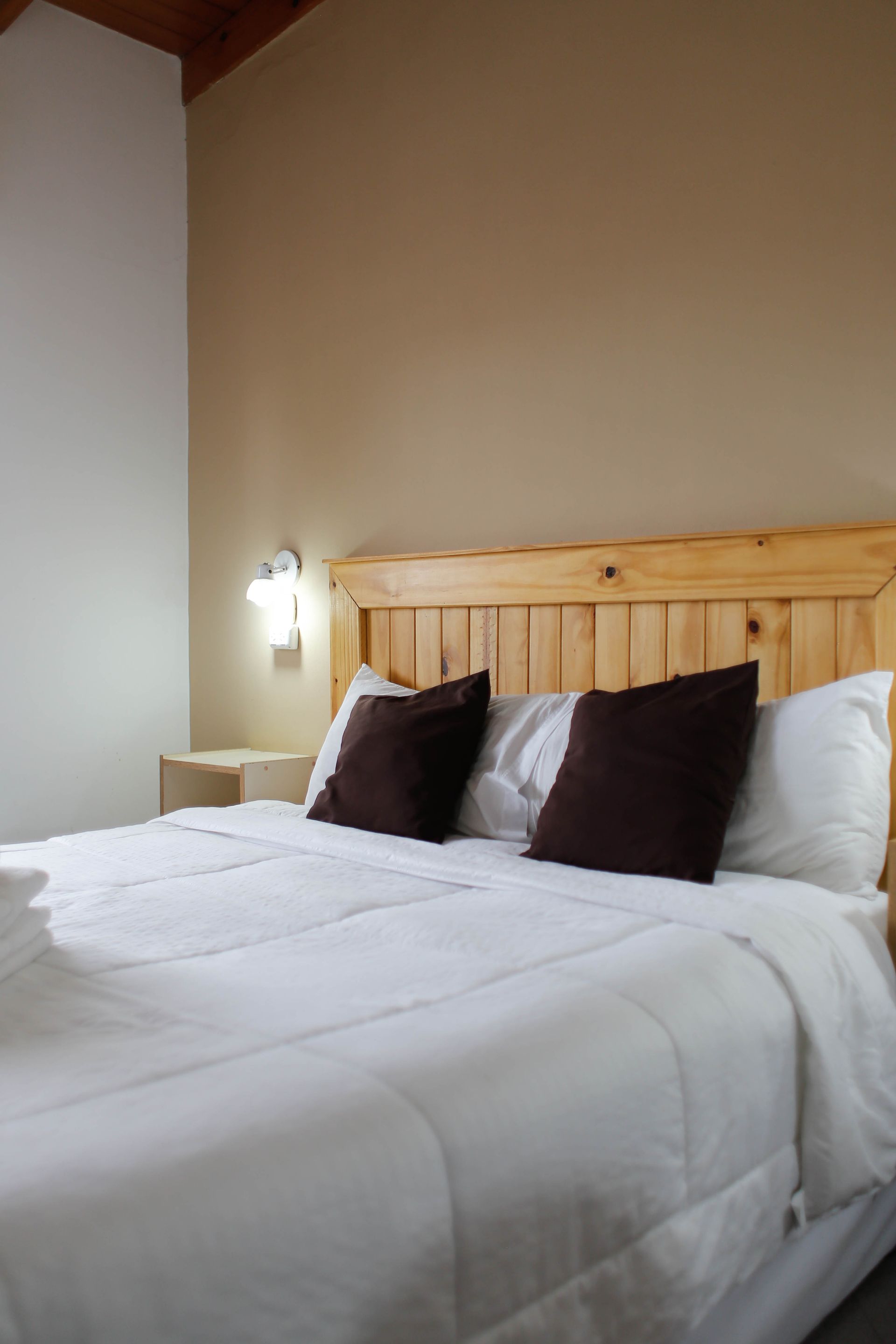 Una cama con sábanas blancas y almohadas marrones en una habitación de hotel
