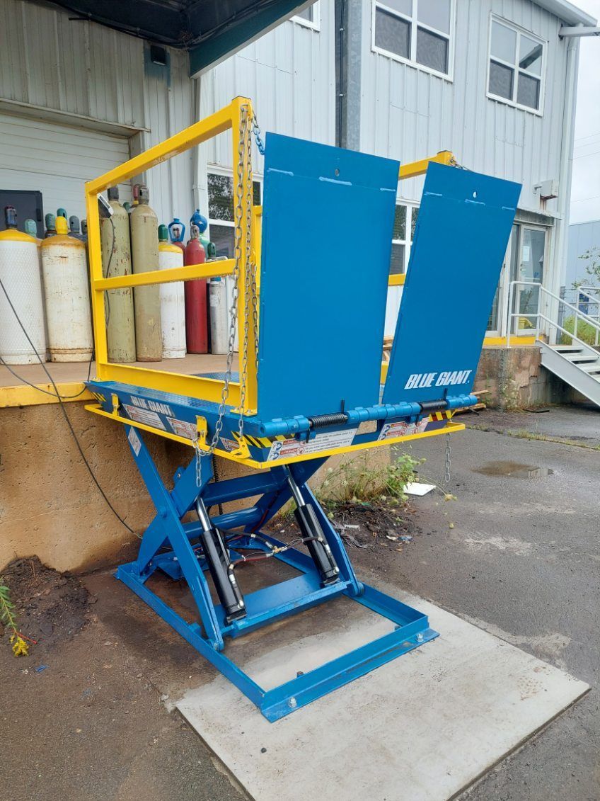 A blue and yellow scissor lift is sitting in front of a building
