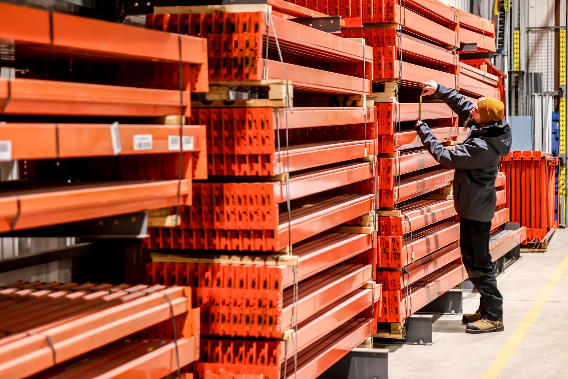 A man is standing in front of a stack of orange shelves in a warehouse.