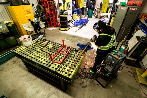 A man is welding a piece of metal in a workshop.