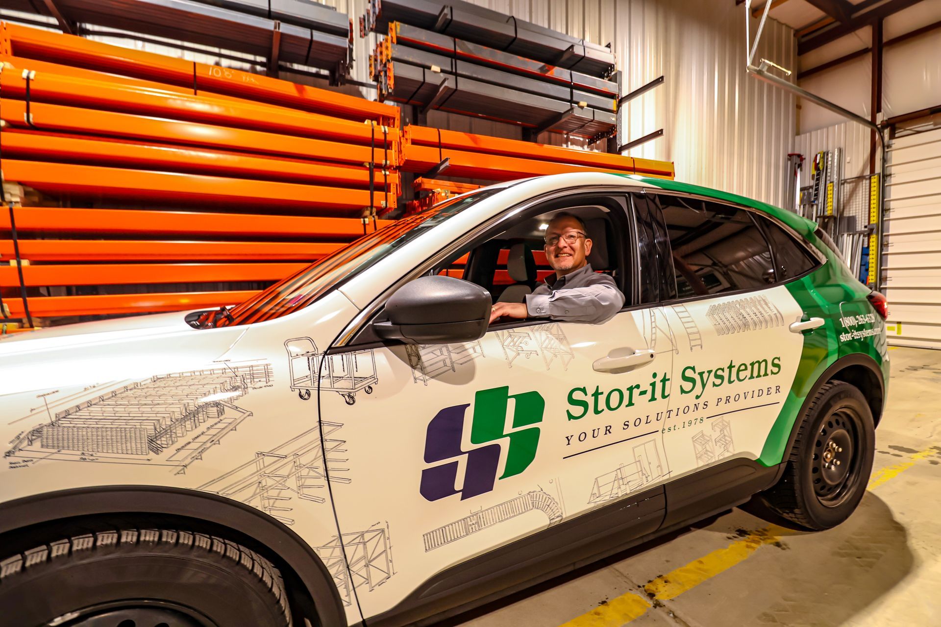 A man is driving a white and green car in a warehouse.