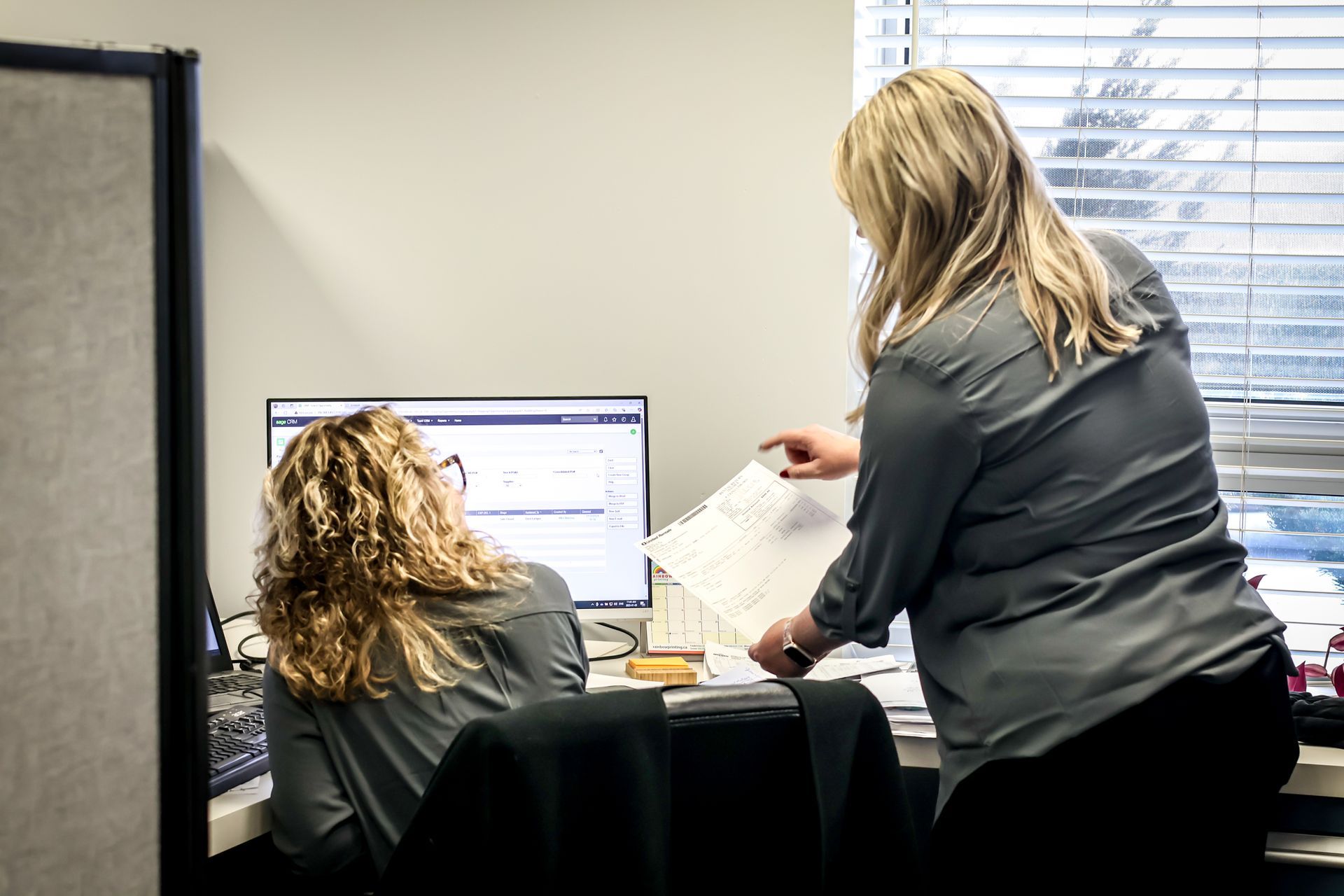 Two women are sitting at a desk in front of a computer.