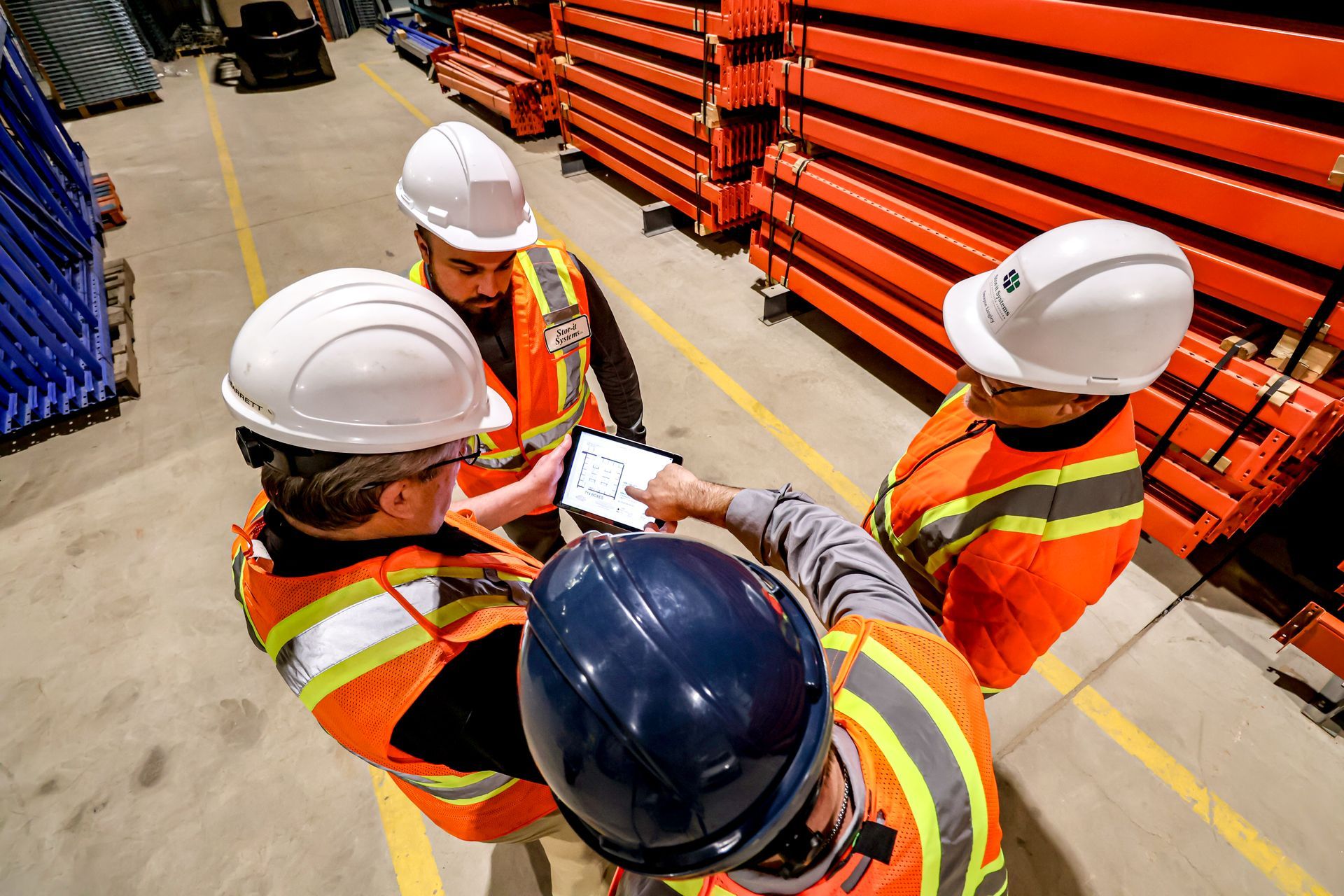 A group of construction workers are standing in a warehouse looking at a tablet.