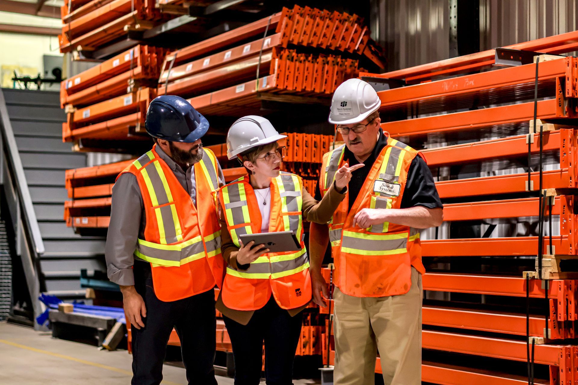 A group of construction workers are standing in a warehouse looking at a tablet.