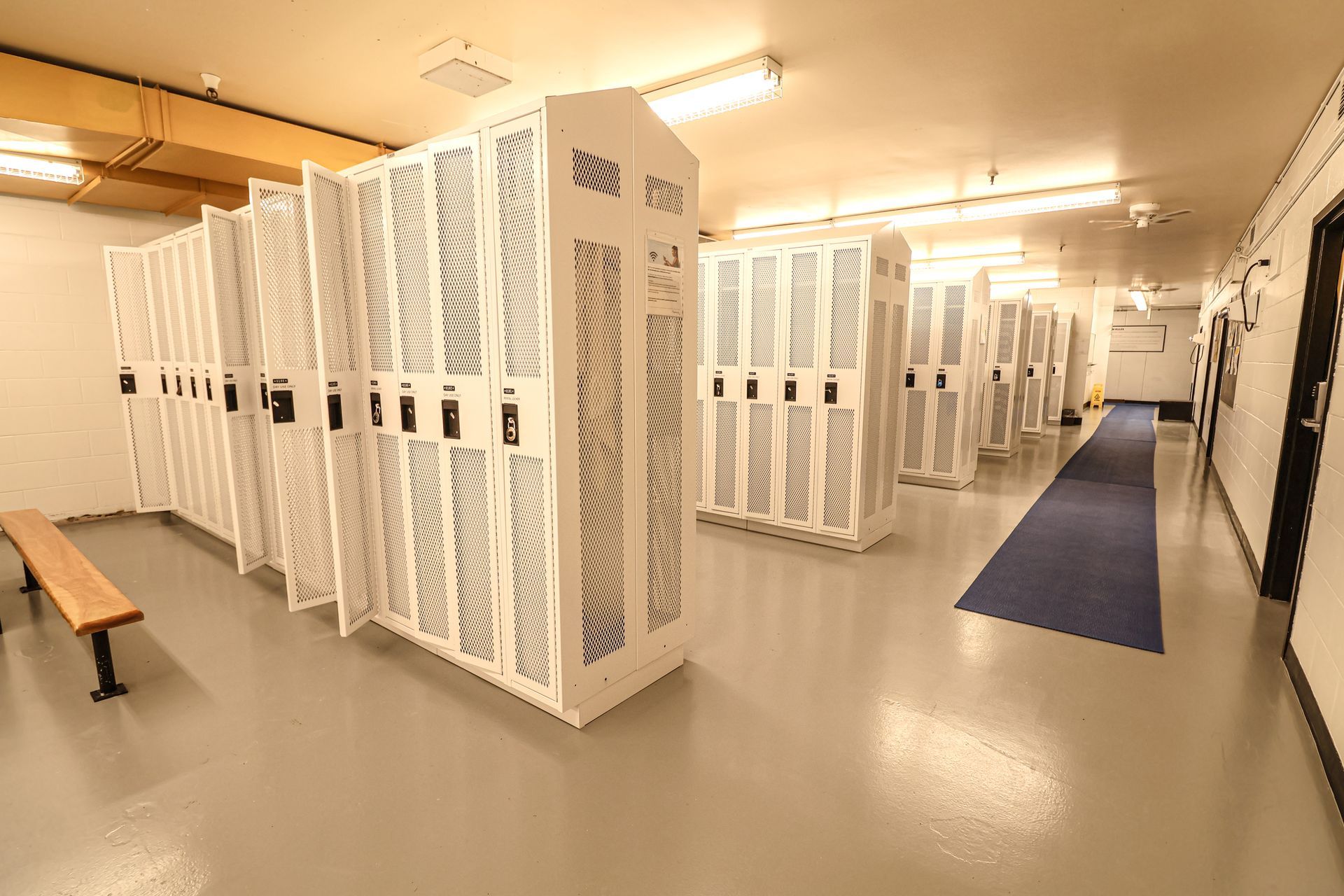 A locker room filled with lots of white lockers and a bench.