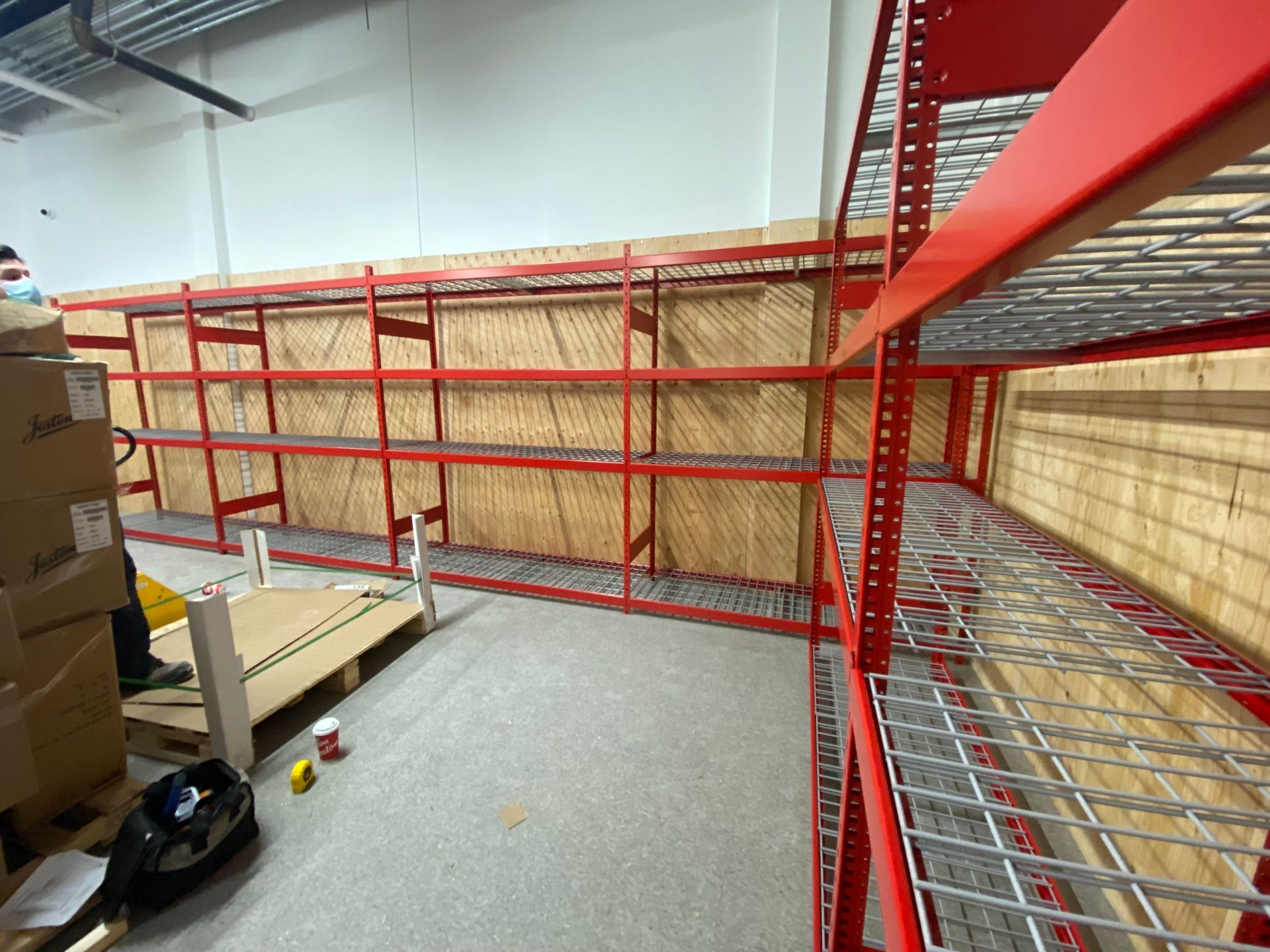 Red metal warehouse mezzanine and shelving beside stacked cardboard boxes and a pallet.