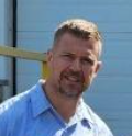 A man in a blue shirt and white shirt is smiling for the camera.