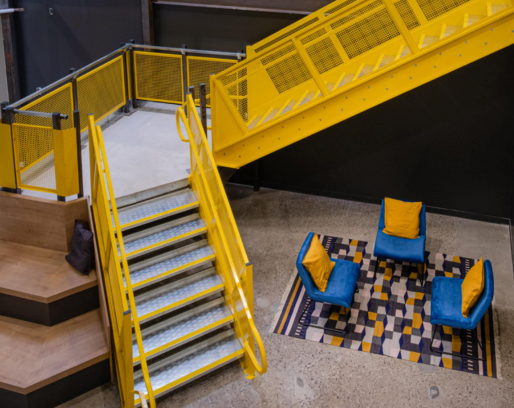 A yellow staircase leading up to a room with chairs and a rug.