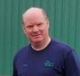 A man in a blue shirt is standing in front of a green wall.