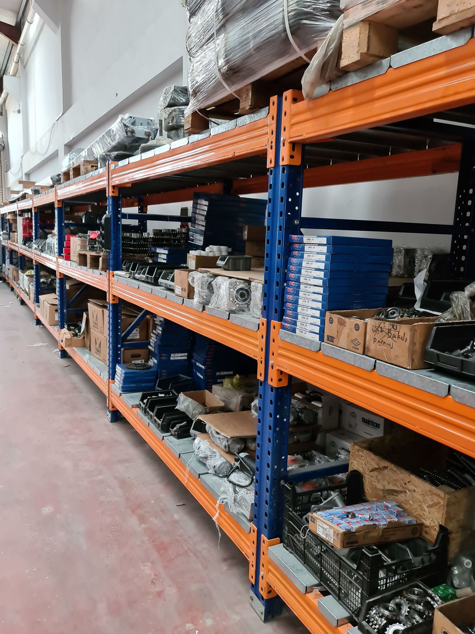 Warehouse aisle with orange metal shelving stacked with boxes and parts.