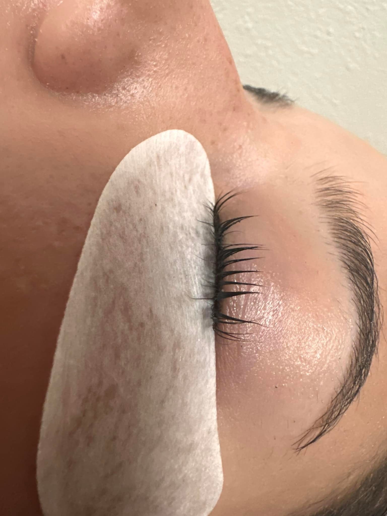 A close-up view of an eyelid with a protective white under-eye patch applied during a professional eyelash procedure.
