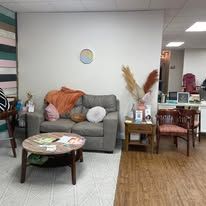 A waiting area with a grey loveseat, a round wooden coffee table, two chairs, and decorative pampas grass on a side table.