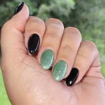 A close-up of a hand with manicured oval nails painted in alternating solid black and shimmering light green.