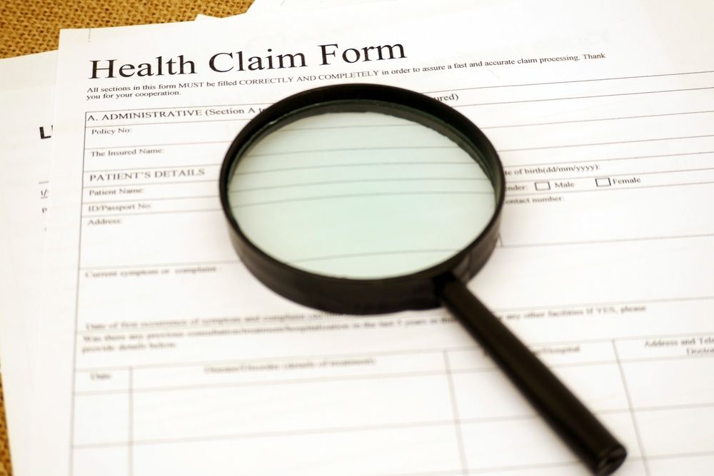 A magnifying glass resting on a health claim form, suggesting document review or insurance fraud investigation.