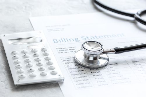A medical billing statement, a stethoscope, and a calculator on a white surface.