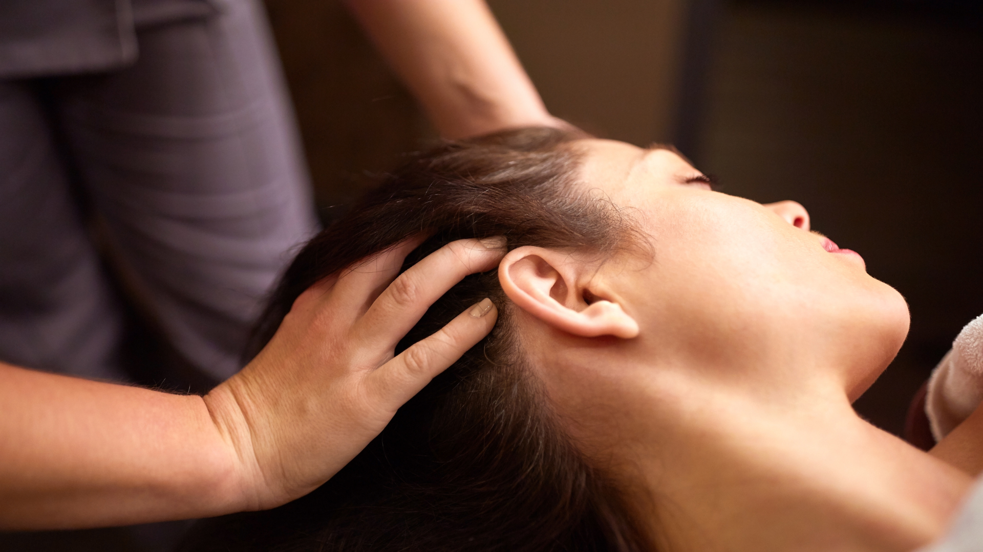 Hand massaging a woman’s head near her ear in a warm indoor setting