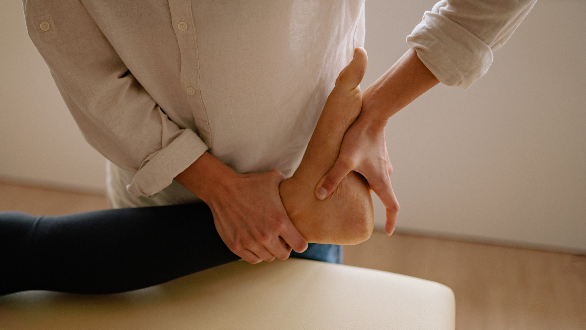 Hands stretching a foot on a massage table, with a blue toe separator in a clinical setting