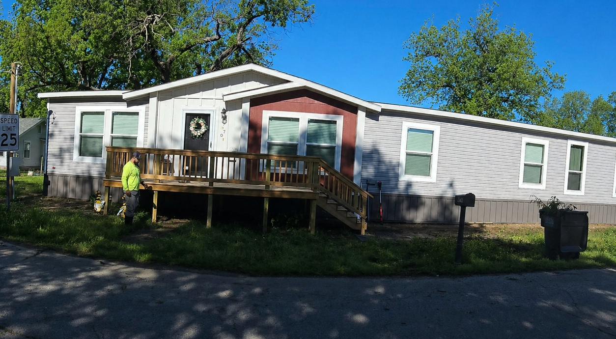 Single-story gray house with a red front entry and wooden porch in a sunny yard