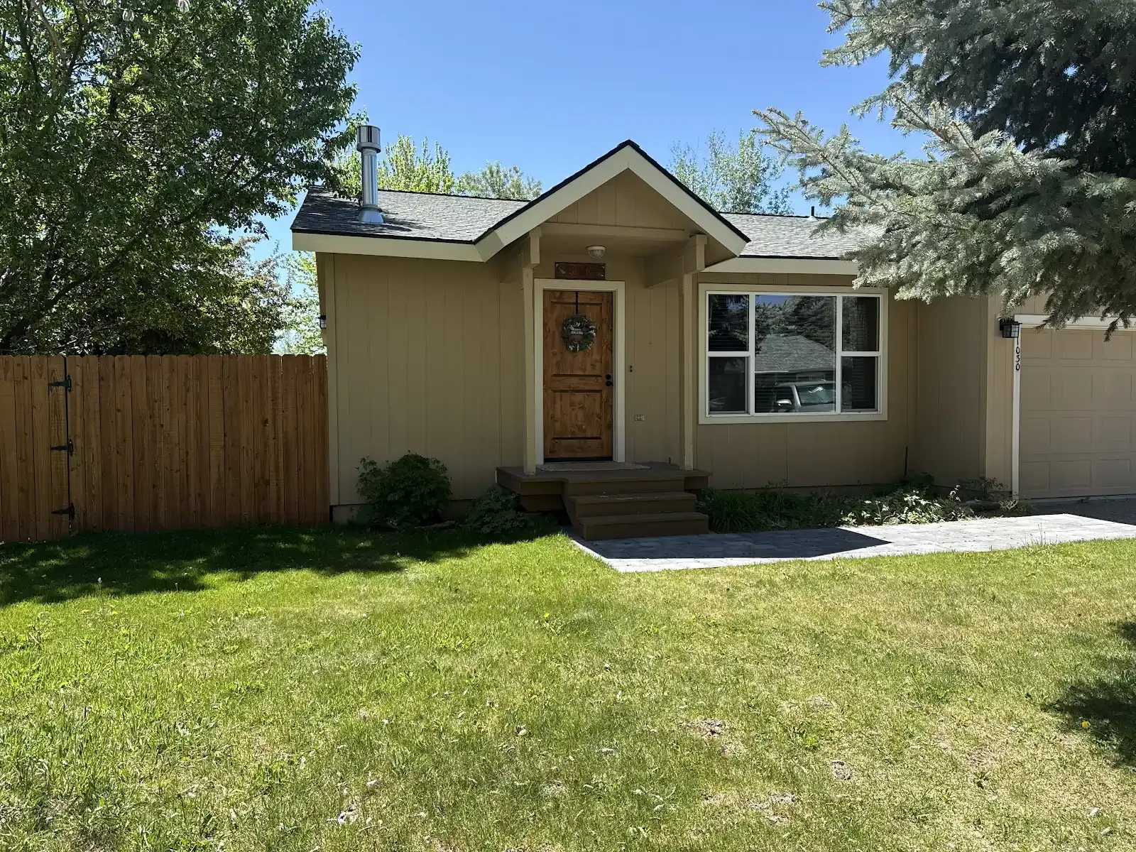 Small tan house with a wooden front door, large window, and green lawn in front