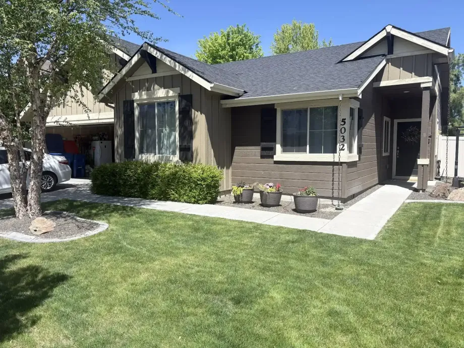 Single-story house with gray siding, manicured lawn, and a concrete walkway under a sunny sky