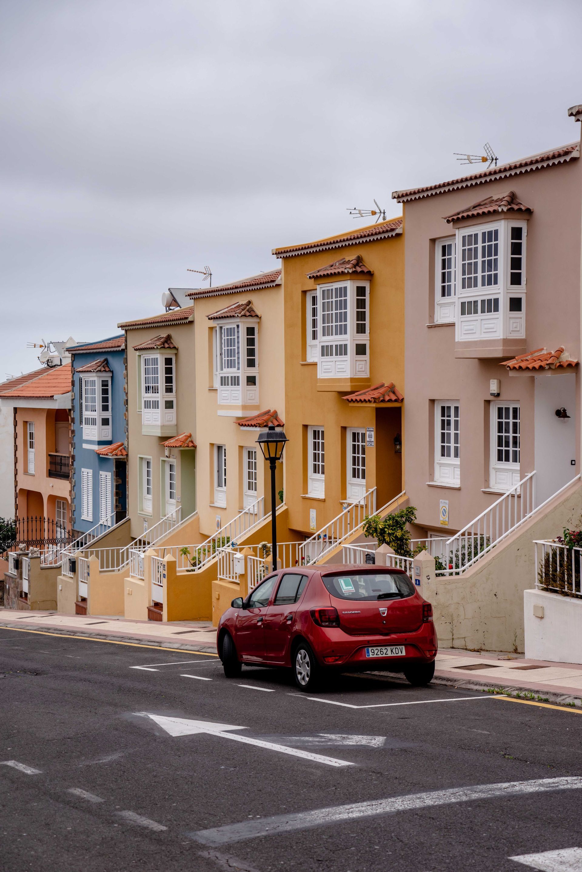 Colorful hillside row houses on a steep street with a red car parked in front.