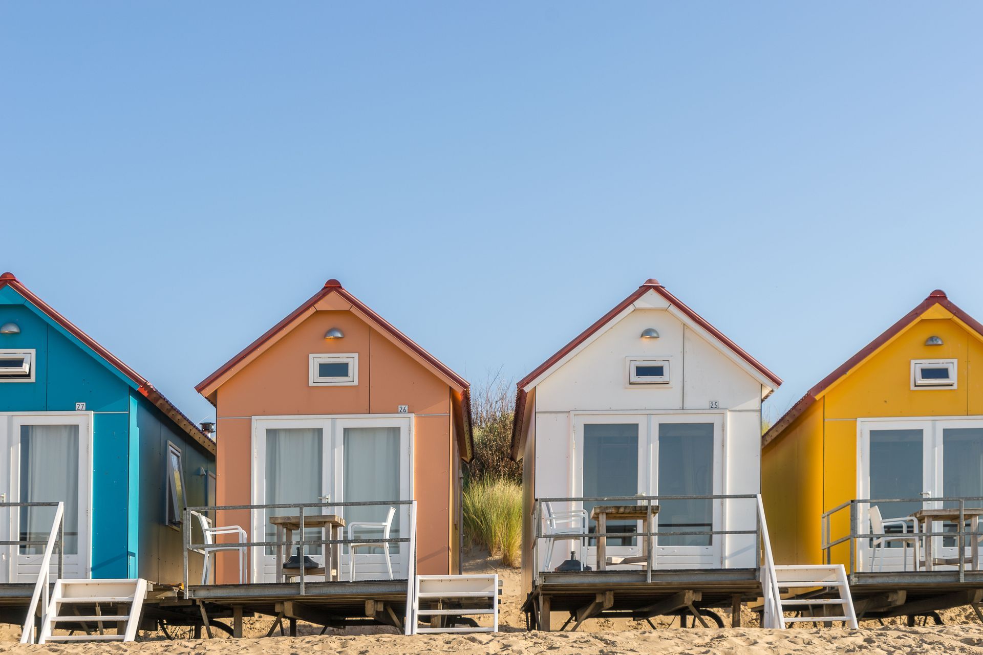 Colorful beach huts lined up on a sandy shore under a clear blue sky.
