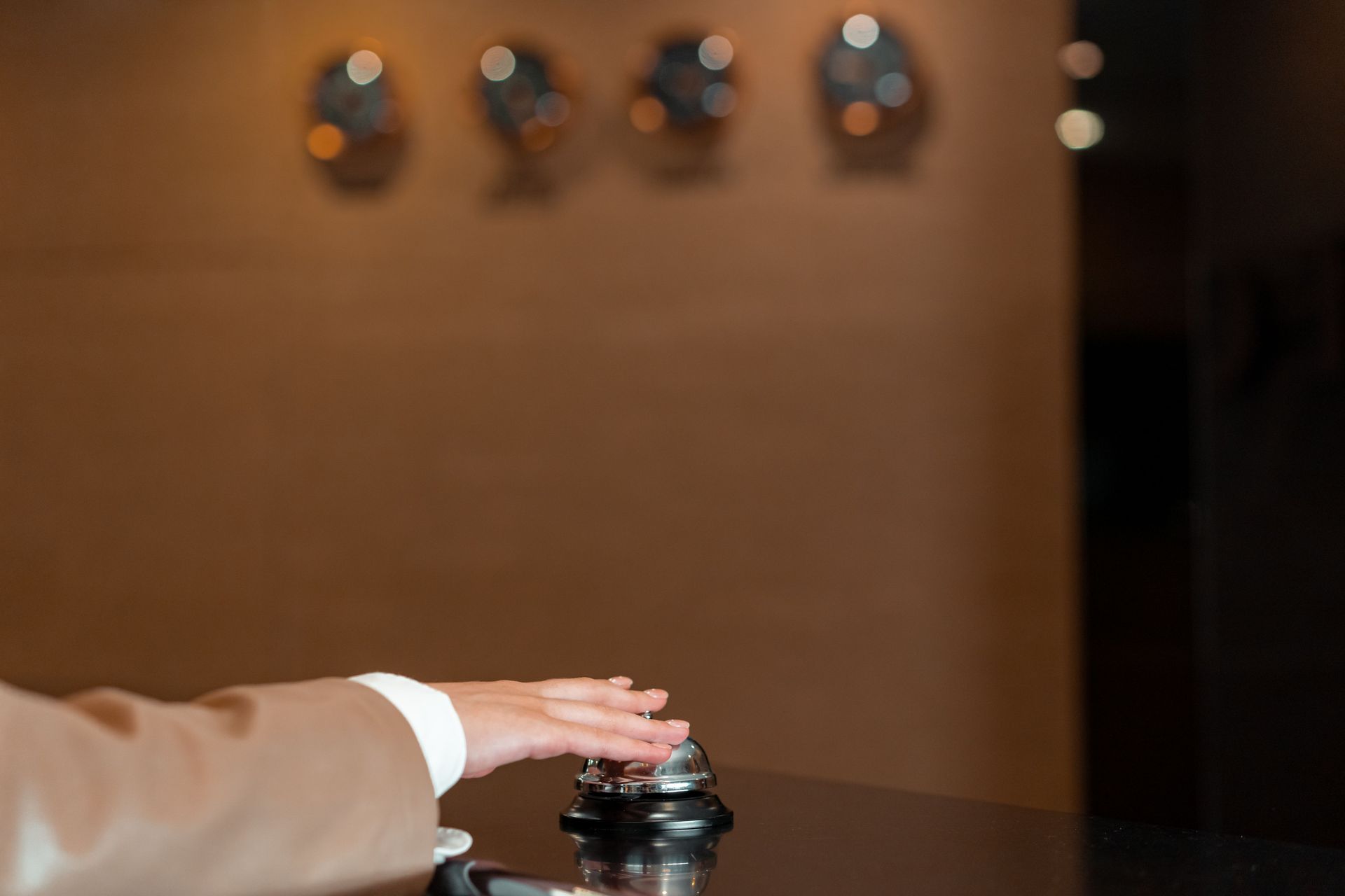 A hand in a beige sleeve reaches for a service bell at a reception desk.
