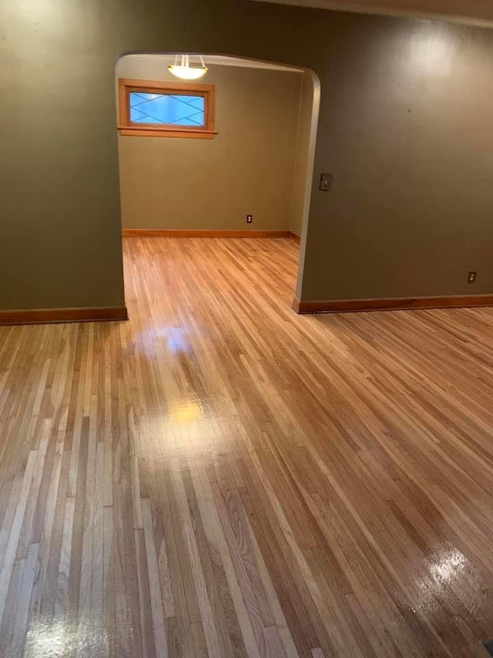 Empty room with glossy hardwood floors, tan walls, and a small window lit by a ceiling lamp.
