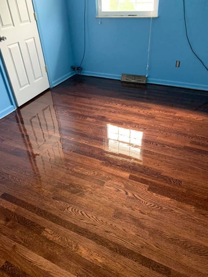 Empty blue room with glossy dark hardwood floor and a window reflecting light.
